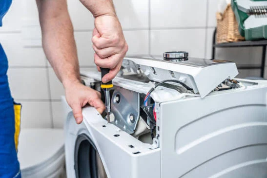 Hands using a screwdriver on an opened laundry-appliance top panel